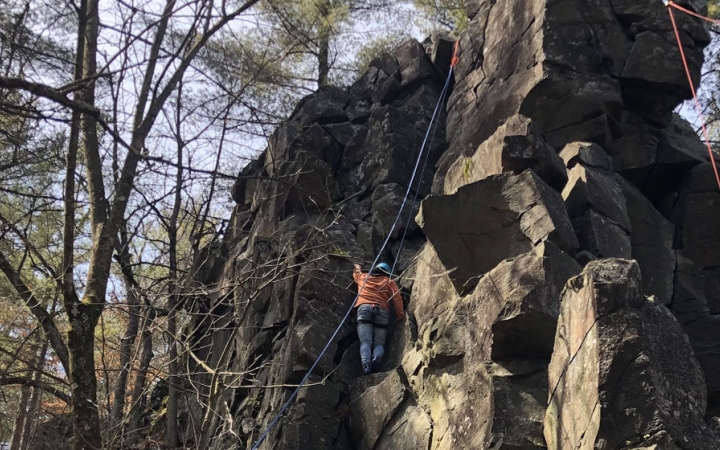 A person wearing safety gear is secured by ropes as they climb up a rock formation.
